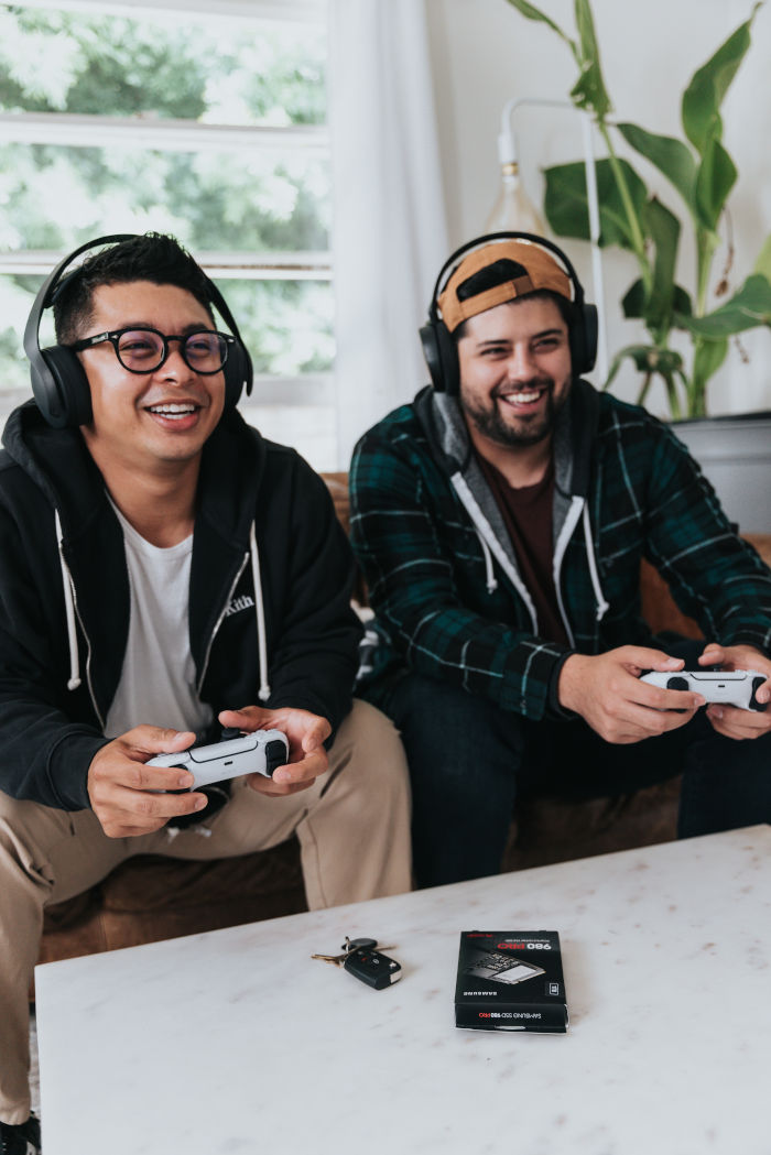 Zwei Männer spielen mit Gamecontrollern und Kopfhörern auf einer Couch